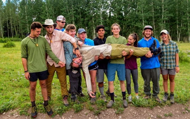a group of gap year students hold up one person who is laying across their hands
